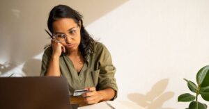 (stressed woman holding a credit card in front of her laptop)