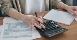 (Person using a calculator with financial documents and a notebook, representing debt tracking and personal finance management.)