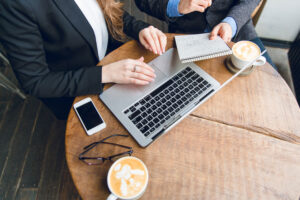 Close-up of two people sitting at a table with their hands clasped, surrounded by financial documents, a smartphone, and a leather portfolio